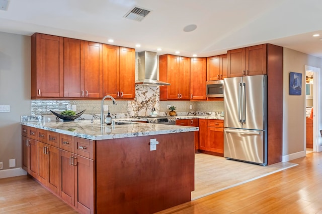 kitchen featuring wall chimney range hood, appliances with stainless steel finishes, light stone countertops, and light wood-type flooring