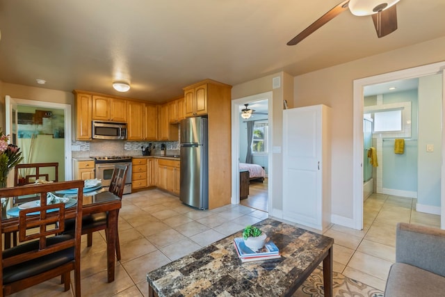 kitchen featuring light tile patterned flooring, appliances with stainless steel finishes, dark stone counters, ceiling fan, and decorative backsplash