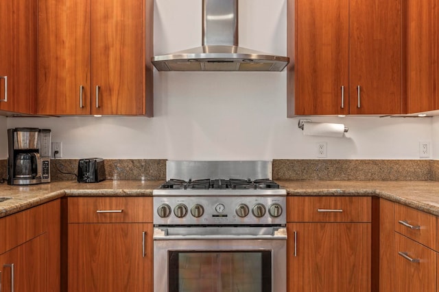 kitchen with stainless steel stove, wall chimney exhaust hood, and light stone counters