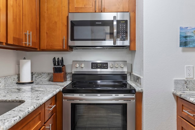 kitchen featuring stainless steel appliances, brown cabinets, light stone countertops, and a textured wall