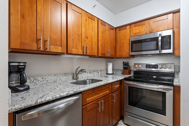 kitchen featuring appliances with stainless steel finishes, a sink, light stone counters, and brown cabinetry