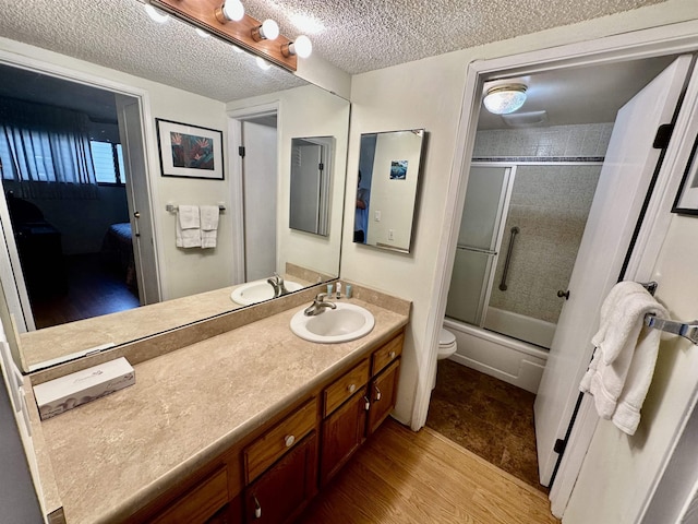 full bathroom featuring hardwood / wood-style floors, vanity, shower / bath combination with glass door, toilet, and a textured ceiling