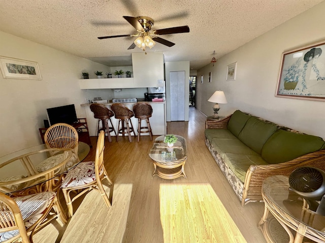 living room with ceiling fan, light wood-type flooring, and a textured ceiling