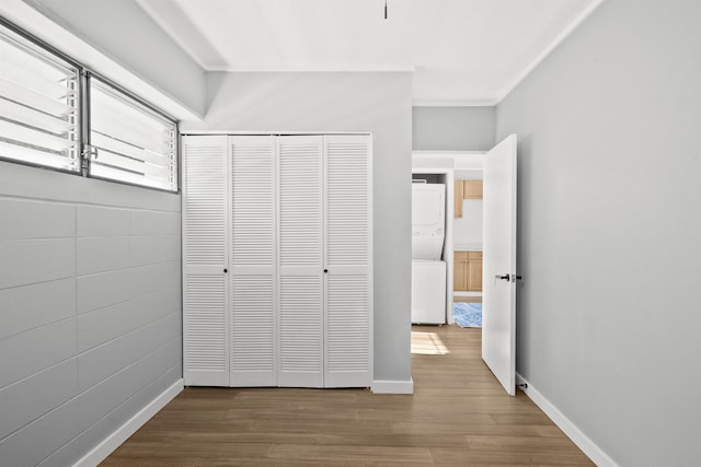 unfurnished bedroom with stacked washer / dryer, crown molding, a closet, and wood-type flooring