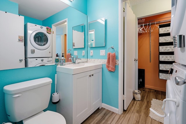 bathroom with stacked washer / dryer, vanity, hardwood / wood-style floors, and toilet