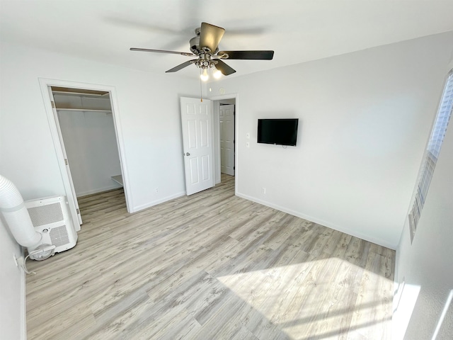 unfurnished bedroom featuring light hardwood / wood-style flooring, a closet, a walk in closet, and ceiling fan