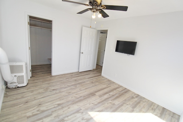 unfurnished bedroom with a spacious closet, a closet, light hardwood / wood-style floors, and ceiling fan