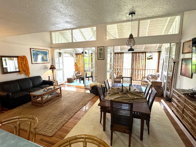 dining space with high vaulted ceiling, a textured ceiling, and hardwood / wood-style flooring