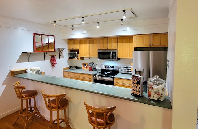 kitchen with kitchen peninsula, a breakfast bar, stainless steel appliances, rail lighting, and hardwood / wood-style flooring