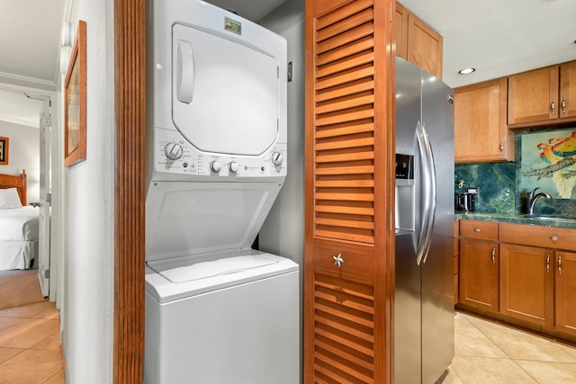 laundry room featuring stacked washer and clothes dryer, crown molding, light tile patterned flooring, a sink, and laundry area