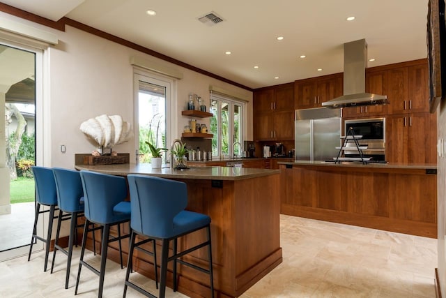 kitchen featuring a breakfast bar, built in appliances, ornamental molding, kitchen peninsula, and island exhaust hood