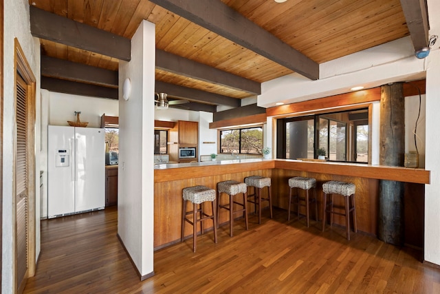 kitchen with beamed ceiling, wood ceiling, dark hardwood / wood-style floors, white refrigerator with ice dispenser, and a kitchen breakfast bar