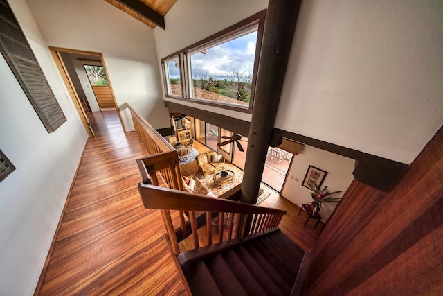 stairway featuring wood-type flooring, beam ceiling, and high vaulted ceiling