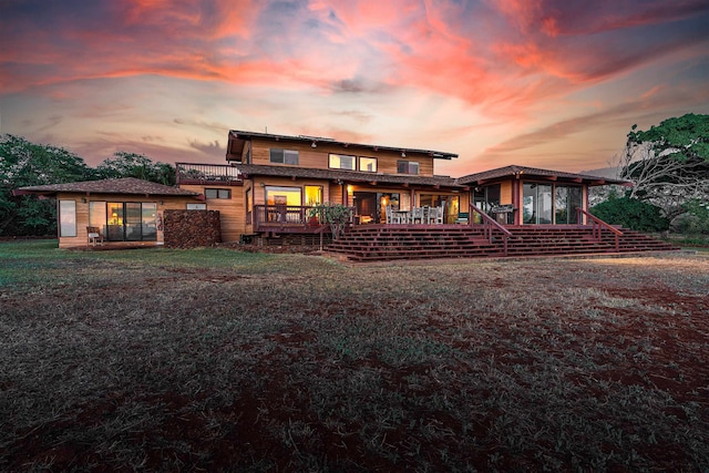 back house at dusk featuring a wooden deck and a lawn