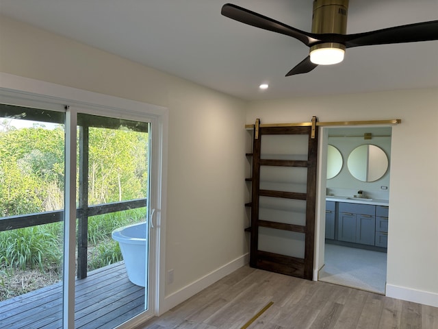 interior space with baseboards, light wood-style flooring, ceiling fan, a sink, and a barn door