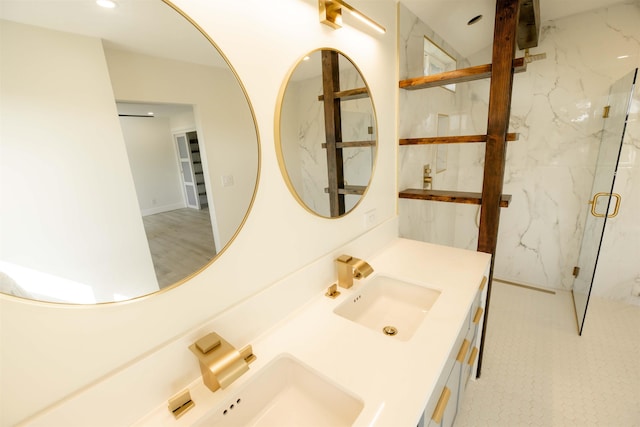 full bath with a marble finish shower, double vanity, and a sink