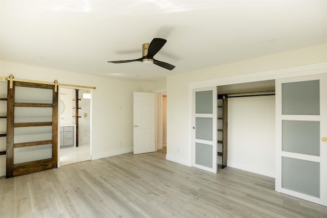 unfurnished bedroom with baseboards, a barn door, wood finished floors, a closet, and a ceiling fan