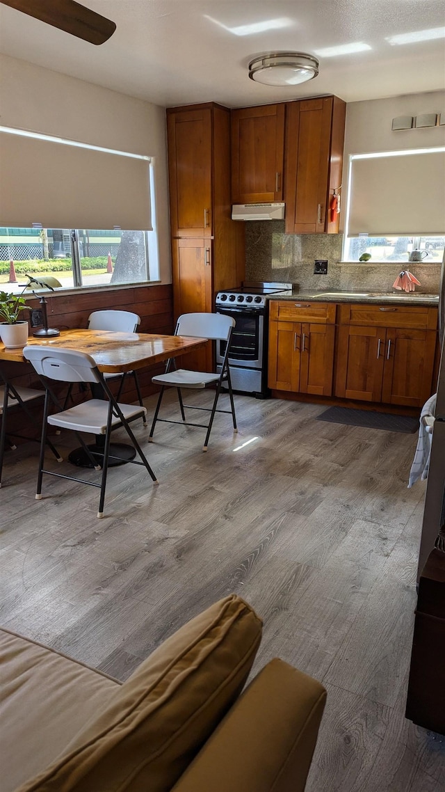 kitchen with backsplash, light hardwood / wood-style flooring, ceiling fan, and stainless steel range with electric cooktop