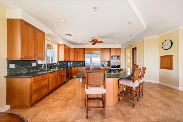 kitchen featuring ceiling fan, sink, built in appliances, a breakfast bar, and a kitchen island