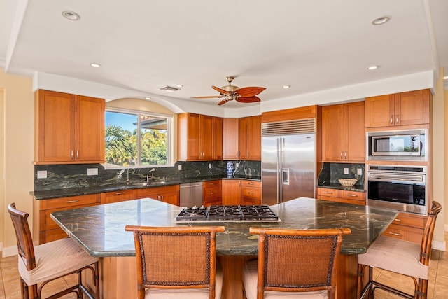 kitchen featuring a kitchen bar, ceiling fan, a spacious island, sink, and built in appliances