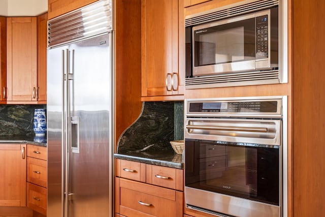 kitchen featuring built in appliances, dark stone counters, and backsplash