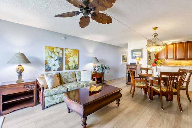 living room with ceiling fan, a textured ceiling, and light hardwood / wood-style flooring