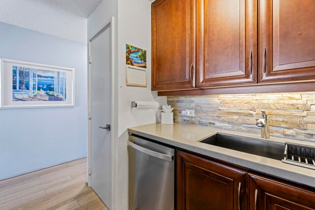 kitchen featuring sink, backsplash, stainless steel dishwasher, light hardwood / wood-style floors, and a textured ceiling