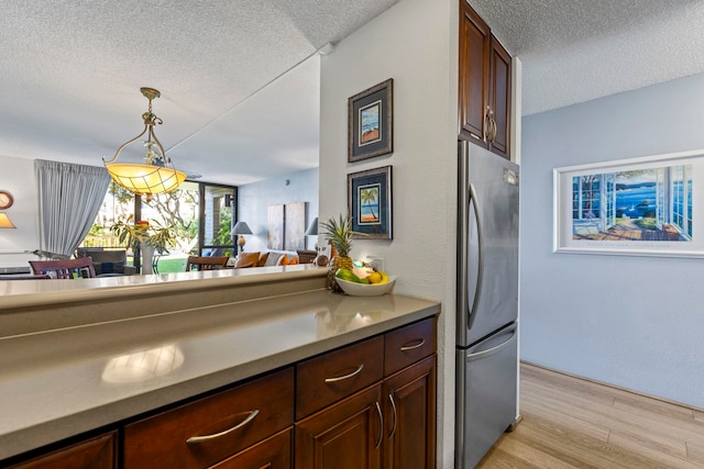 kitchen featuring light hardwood / wood-style floors, a textured ceiling, stainless steel refrigerator, and decorative light fixtures