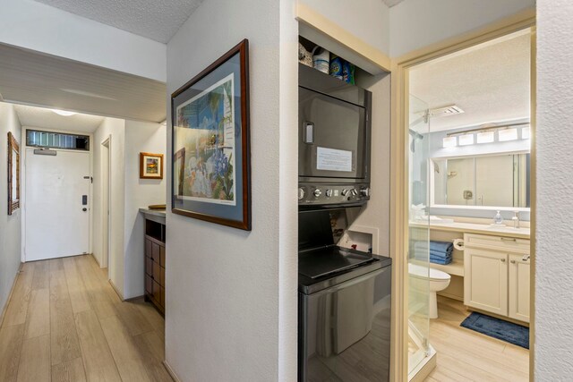 hallway featuring light hardwood / wood-style flooring, a textured ceiling, and stacked washer / dryer