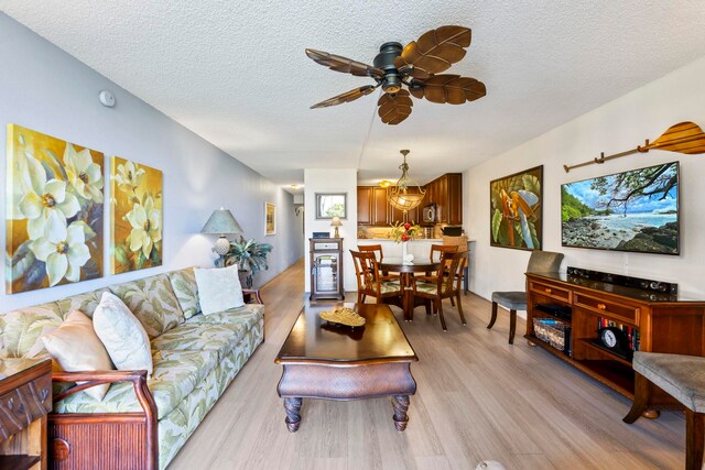 living room with ceiling fan, a textured ceiling, and light wood-type flooring