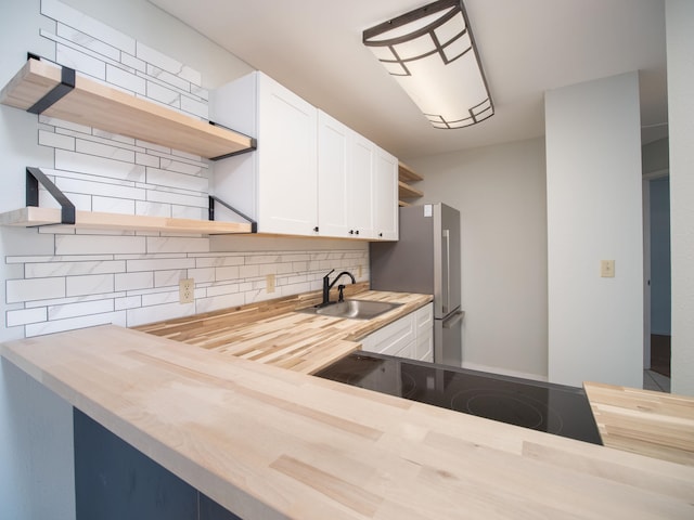 kitchen with tasteful backsplash, stainless steel fridge, butcher block counters, sink, and white cabinetry