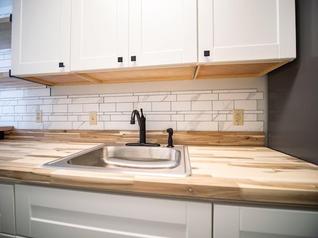 room details featuring wood counters, sink, tasteful backsplash, and white cabinetry