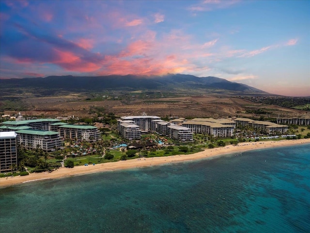 aerial view at dusk featuring a view of the beach and a water and mountain view