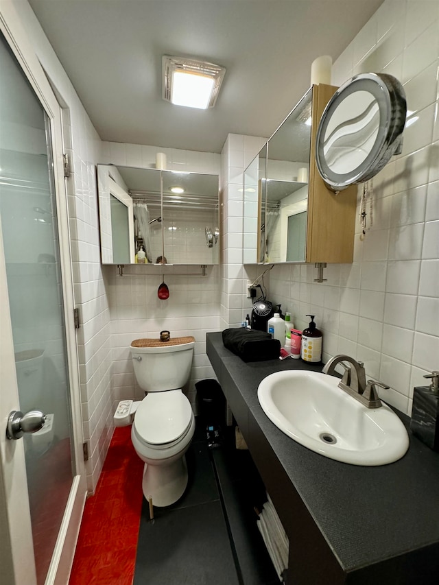 bathroom with vanity, tile walls, toilet, and a shower with shower door