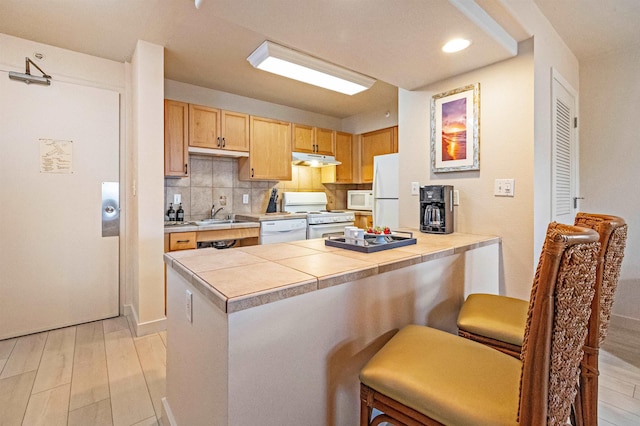 4327 Lower Honoapiilani Rd Unit 101B, Lahaina, HI 96761 - kitchen featuring white appliances, under cabinet range hood, a peninsula, a kitchen bar, and backsplash
