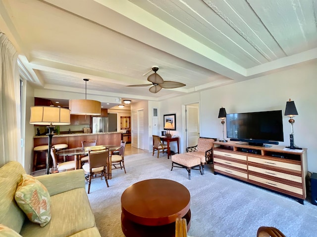 carpeted living room with ceiling fan, a raised ceiling, and beamed ceiling