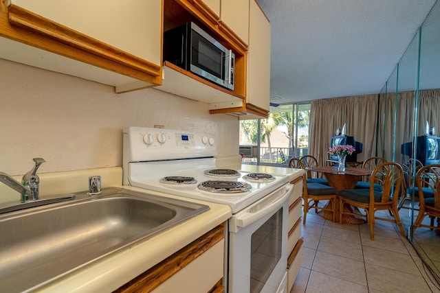 kitchen with light tile patterned floors, white electric range, white cabinetry, and sink