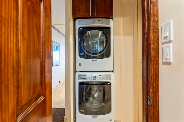 clothes washing area featuring tile patterned floors, stacked washer and dryer, and cabinets