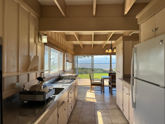 kitchen with light tile flooring, beamed ceiling, a notable chandelier, a water view, and white refrigerator