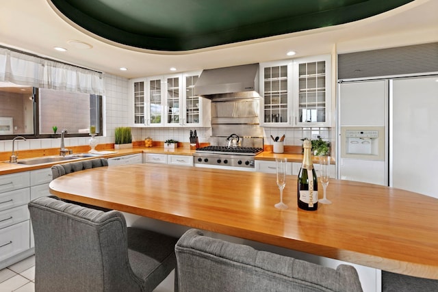 kitchen with white cabinetry, wall chimney range hood, sink, and wooden counters