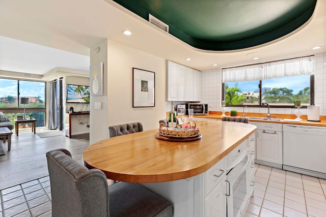 kitchen with a raised ceiling, white cabinetry, dishwasher, and tasteful backsplash