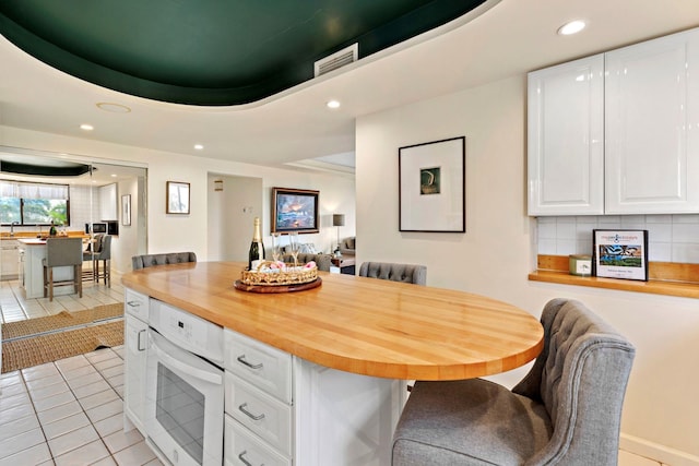 kitchen featuring wood counters, tasteful backsplash, light tile patterned floors, a tray ceiling, and white cabinets