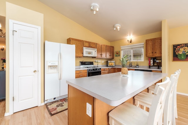 kitchen featuring a breakfast bar, vaulted ceiling, a kitchen island, light hardwood / wood-style flooring, and white appliances