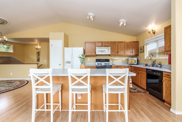 kitchen featuring a kitchen breakfast bar, vaulted ceiling, black appliances, a center island, and sink