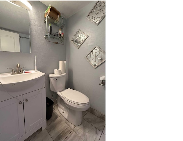 bathroom with a textured wall, baseboards, toilet, and vanity