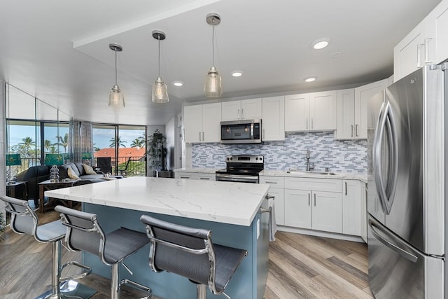 kitchen featuring hanging light fixtures, white cabinets, appliances with stainless steel finishes, light hardwood / wood-style floors, and sink