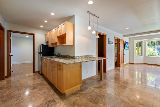 kitchen featuring kitchen peninsula, light stone countertops, light brown cabinets, and decorative light fixtures