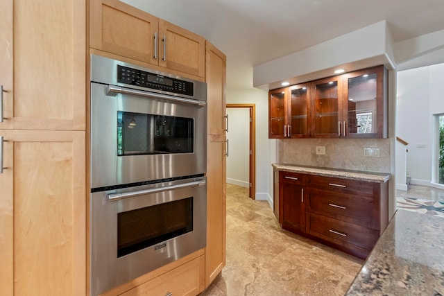 kitchen with light stone counters, stainless steel double oven, and backsplash