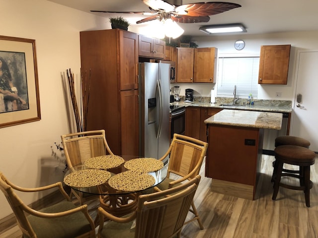 kitchen featuring stainless steel refrigerator with ice dispenser, sink, a kitchen island, range with electric cooktop, and light stone countertops