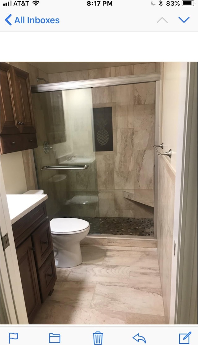 bathroom featuring a shower with door, vanity, and toilet